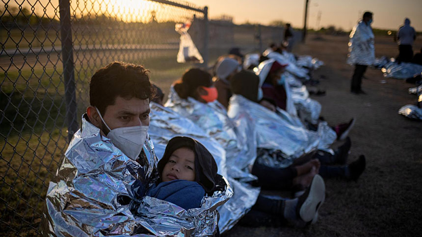 An asylum-seeker from Honduras holds his 6-year-old son in La Joya, Texas, March 19, 2021, as they awake near a baseball field after crossing the Rio Grande. Emergency blankets were provided to the group of about 150 migrants from Central America by Border Patrol agents. (CNS photo/Adrees Latif, Reuters)