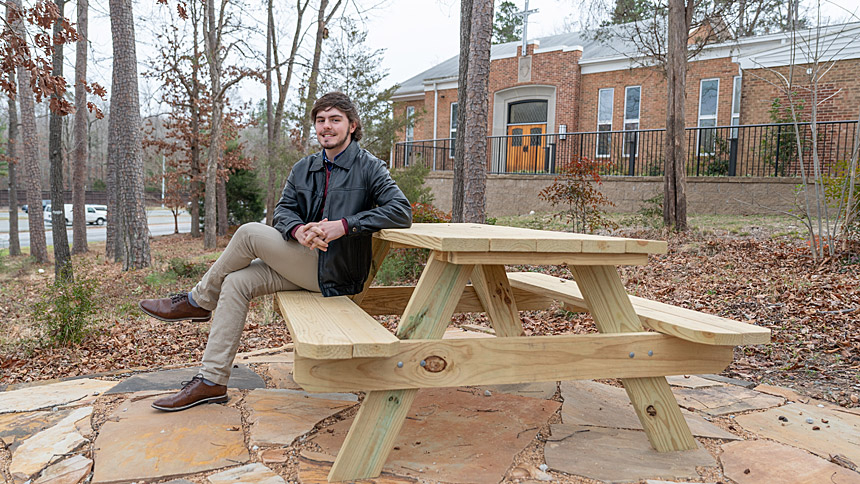 Trevor McNeil sits in a picnic area he helped create for the St. Thomas More community. (Photo by Maya Reagan)