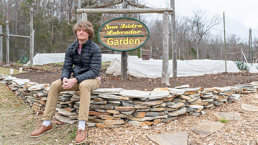 Logan McNeil sits on the retaining wall he helped create for the St. Thomas More Community. (Photo by Maya Reagan)