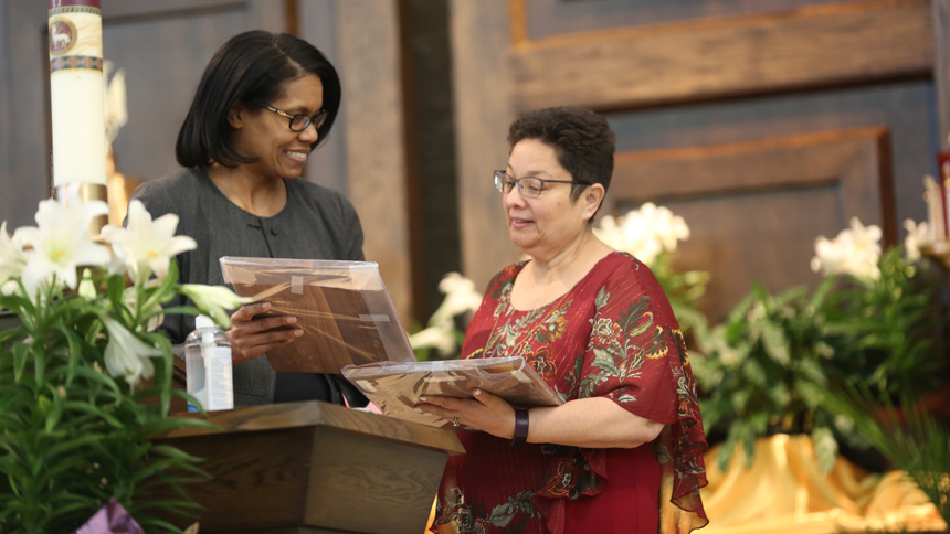 Lytia Reese (left), superintendent of Diocese of Raleigh Catholic Schools, presents two Lewis Award plaques to Maria Gomez, principal of Blessed Sacrament School.