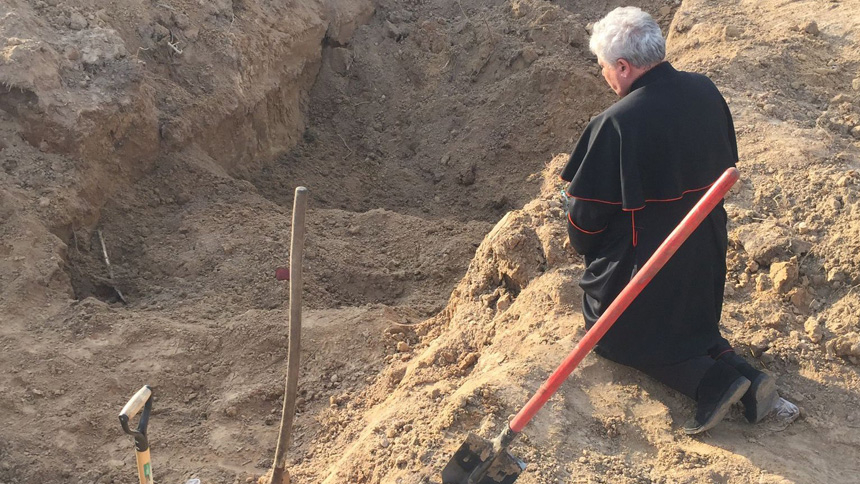 Cardinal Konrad Krajewski, the papal almoner, prays over a mass grave near Borodyanka, Ukraine, April 15, 2022. During a mid-September visit to Ukraine as an envoy of Pope Francis, he visited a mass grave in Izium, Ukraine. (CNS photo/Vatican Media)