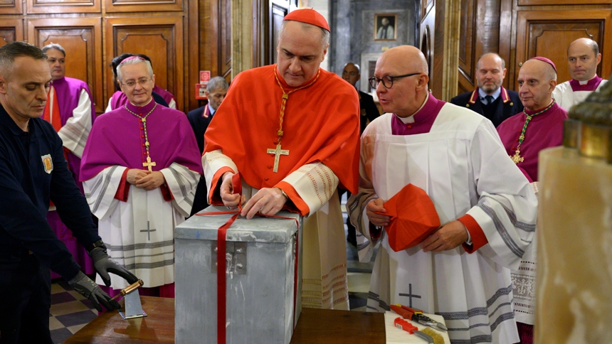 Cardinal Mauro Gambetti, the archpriest of St. Peter's Basilica at the Vatican, unties the ribbons around a box that had been cemented into the Holy Door at the basilica at the end of the Jubilee of Mercy in 2016 during a ceremony in a meeting room at the basilica Dec. 2, 2024. The box was removed in preparation for Pope Francis opening the Holy Door Dec. 24. (CNS photo/Vatican Media)