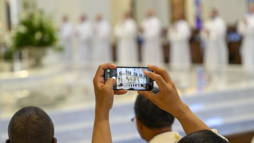 A priest captures a photo during ordination.