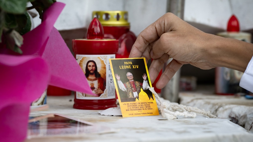 A woman touches some devotional items placed next to a statue of St. John Paul II Oct. 14, 2026, in front of Rome's Gemelli hospital where Pope Leo XIV is recovering from surgery during which doctors removed his lower right lung to treat a cancerous tumor. (CNS photo/Cristian Gennari)