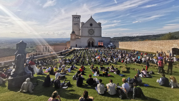 People sit outside the Basilica of St. Francis in Assisi as they attend the beatification Mass of Carlo Acutis in Assisi, Italy, Oct. 10. The Mass was held inside the basilica but measures to prevent the spread of COVID-19 meant that most of the attendees sat outside. (CNS photo/Junno Arocho Esteves)