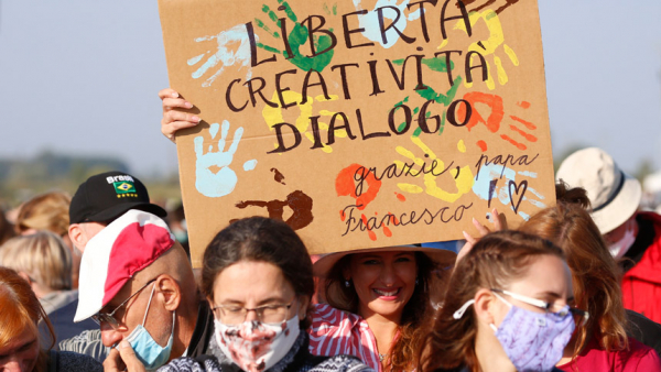  woman holds a sign in Italian reading "Liberty, Creativity and Dialogue" as people wait for Pope Francis' arrival to celebrate Mass on the fields outside the Basilica of Our Lady of Seven Sorrows in Šaštin, Slovakia, Sept. 15, 2021. (CNS photo/Paul Haring)