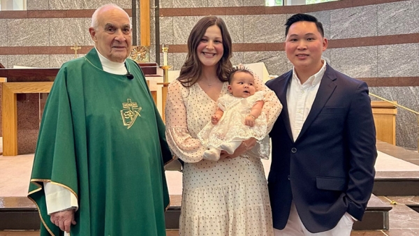 Monsignor Staib stands with Aimee and Peter Nguyen at baby Caroline’s baptism.